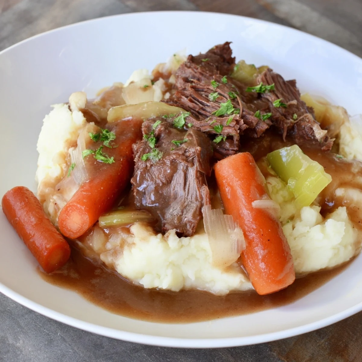 Tender Slow Cooker Pot Roast with vegetables and rich gravy served over fluffy mashed potatoes.