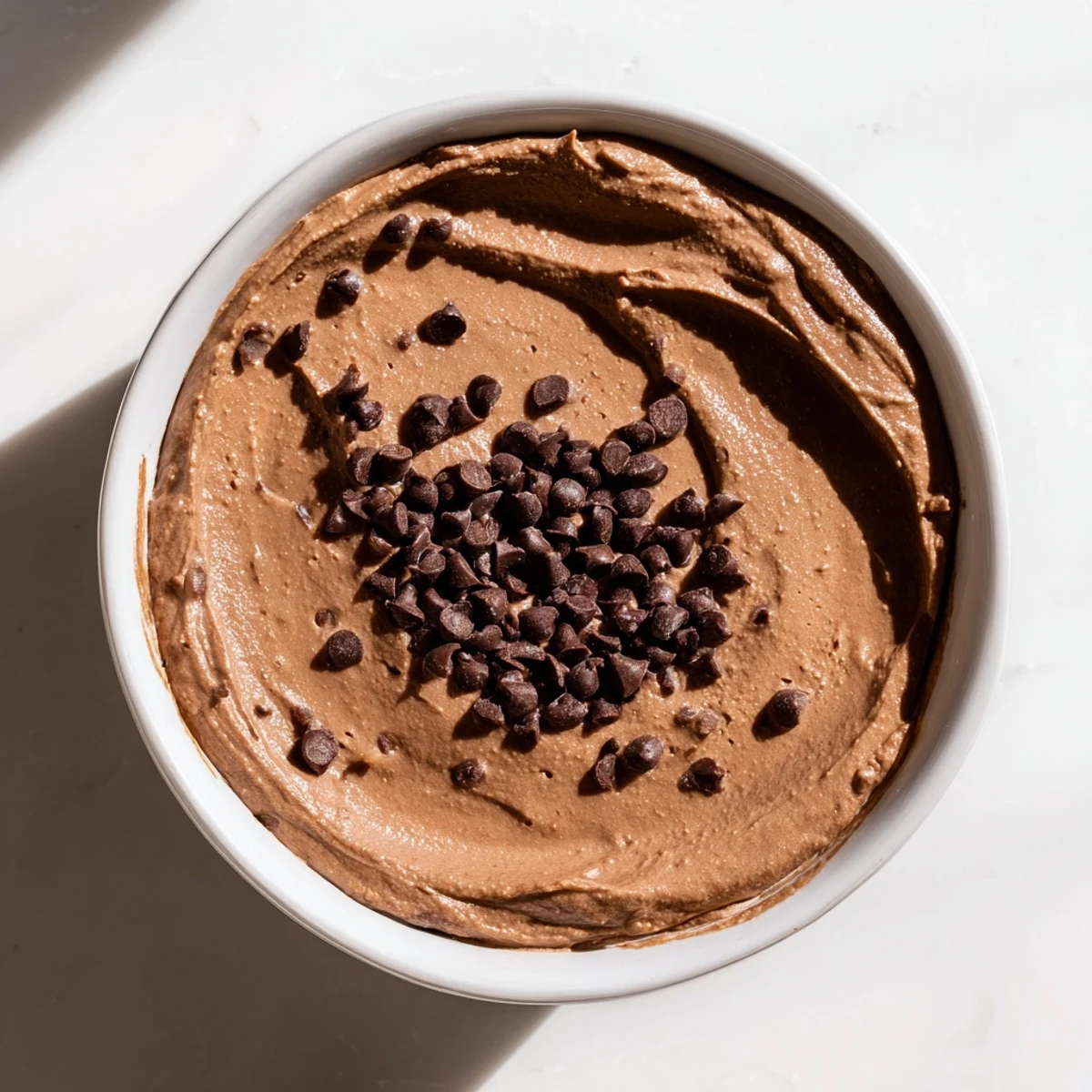 A thick, decadent bowl of chocolate hummus swirled, ready for dipping fruit and crackers.