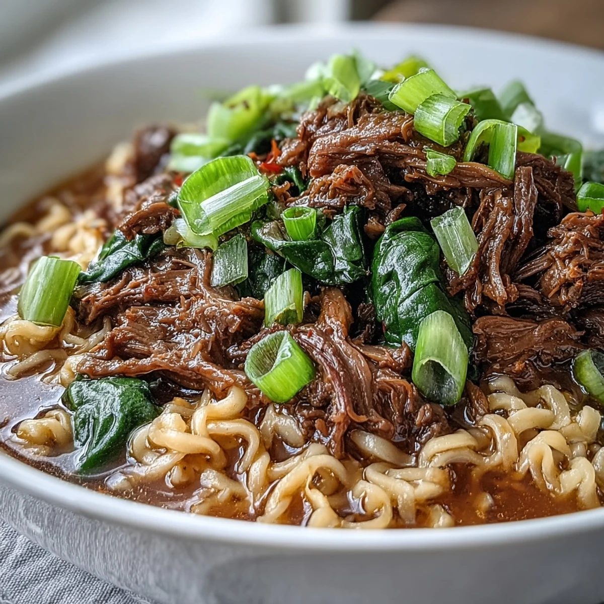 Slow cooker beef ramen noodles with tender shredded beef and a savory broth in a ceramic bowl.