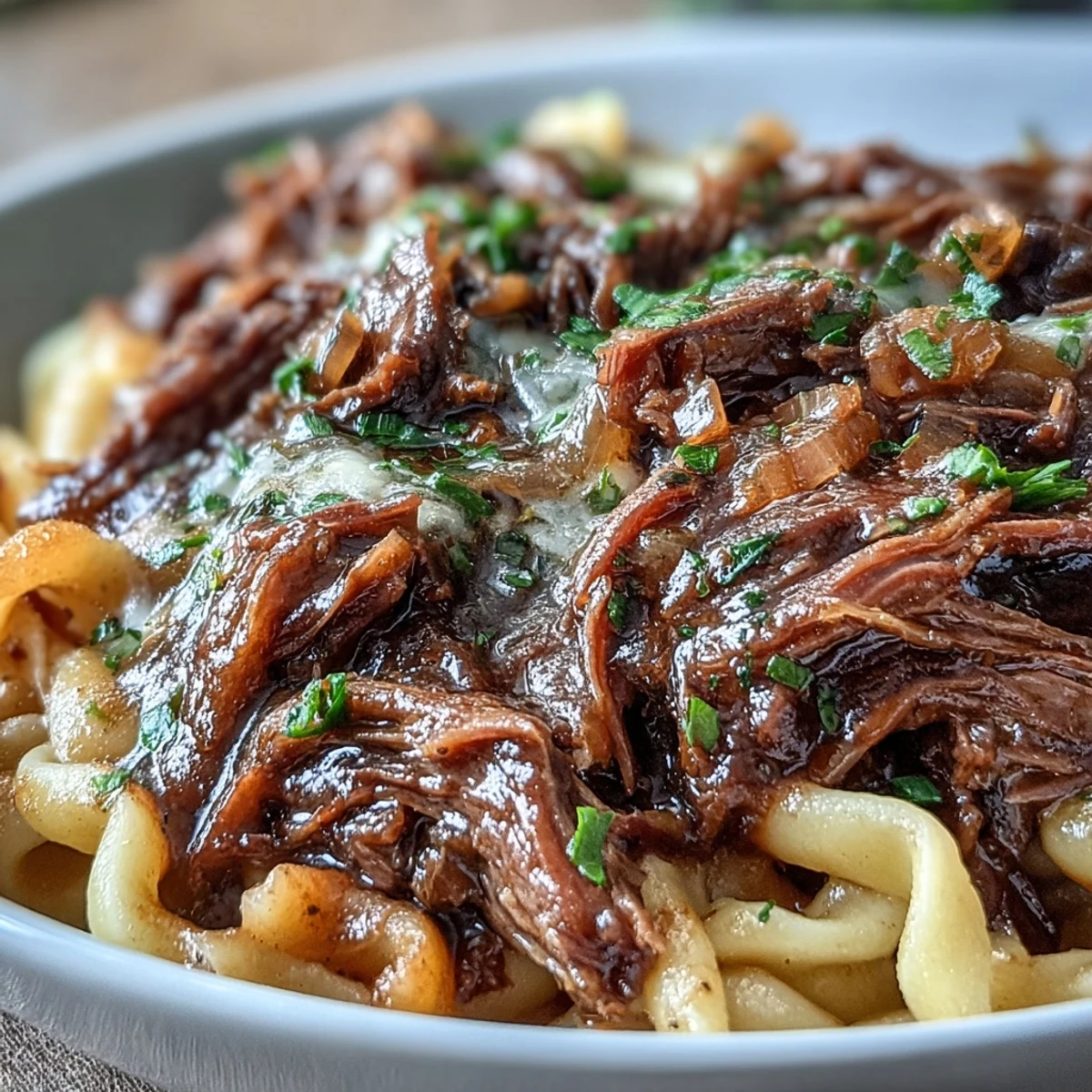 Crockpot French Onion Pot Roast Pasta features tender shredded beef and caramelized onions ladled over buttery egg noodles, garnished with fresh parsley.