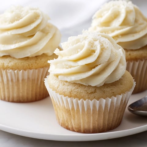 Golden vanilla cupcakes, topped with swirls of creamy frosting, await decoration with sprinkles.