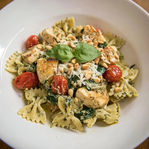 Golden chicken and bowtie pasta with pesto, creamy sauce and fresh basil garnish.