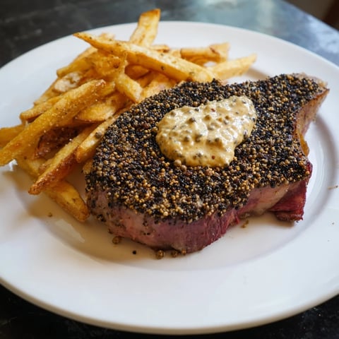 A beautifully plated classic peppercorn ribeye, glistening with peppercorns and served with golden fries.