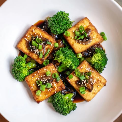 Golden-brown Sautéed Tofu Steak sits alongside vibrant broccoli, shiitakes, and a rich sauce.
