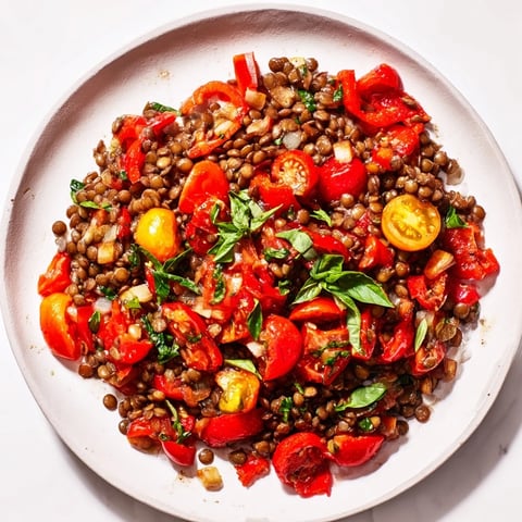 A steaming Lentil-Tomato Skillet, showcasing vibrant red tomatoes with inviting herbs in a pan.