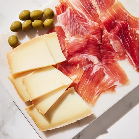 Elegant Minimalism Master cheese board: aged Comté, Iberian ham, and olives arranged beautifully for sharing.