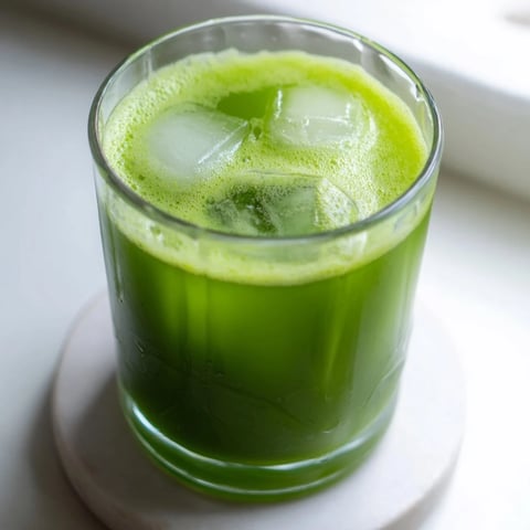 A tall glass of vibrant Cabbage and Kale Detox Juice, garnished with a fresh lemon wedge and glistening with chilled droplets.  