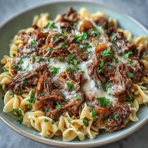 Slow cooker French onion pot roast pasta with tender beef, caramelized onions, and rich gravy served over buttery egg noodles.