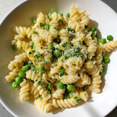 Tender ditalini pasta coated in garlic butter sauce with vibrant green peas in a close up photo.