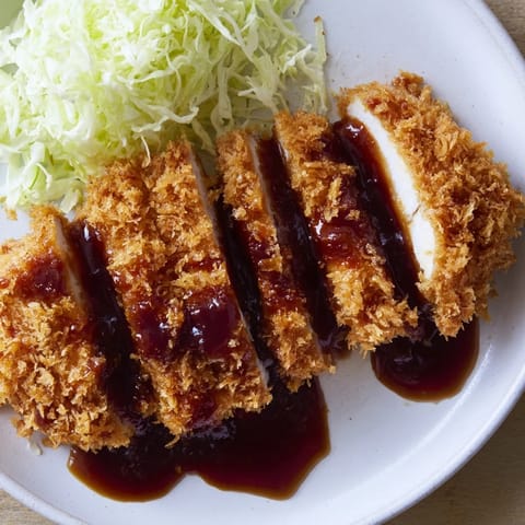 Crispy panko-crusted Chicken Katsu cutlets sit ready, with shredded cabbage and lemon for serving.