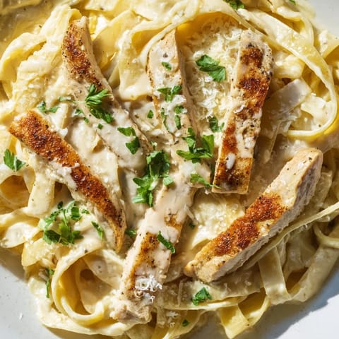 Close-up of fettuccine noodles coated in silky Alfredo sauce, tossed with spiced Cajun chicken and a sprinkle of red pepper flakes.
