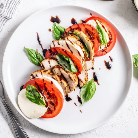 Golden-brown grilled chicken rests atop vibrant tomatoes and fresh basil, with melted mozzarella and a tangy balsamic drizzle in this Chicken Caprese Salad.