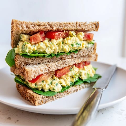 Ripe avocado egg salad sandwich layered with leafy greens and juicy tomato, ready for a healthy, satisfying lunch.