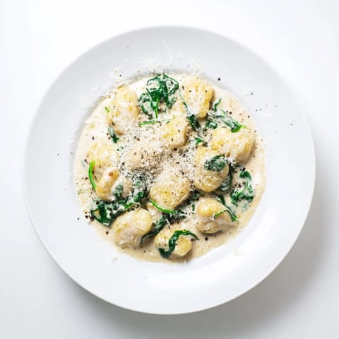 A close-up of Creamy Garlic Gnocchi, highlighting the rich sauce clinging to tender dumplings and wilted greens.  