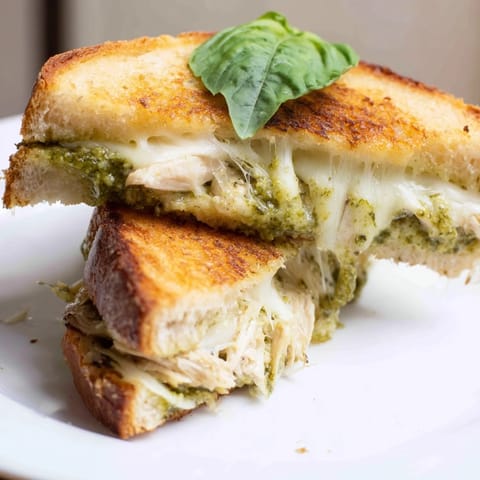 A close-up view shows toasted bread oozing mozzarella and bright green basil pesto spread.
