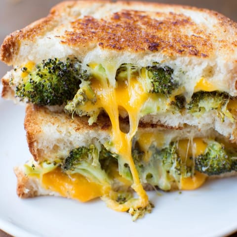 Roasted broccoli and cheddar grilled cheese on buttery toasted bread, melting cheese pulling apart for a delicious dinner sandwich close-up.  