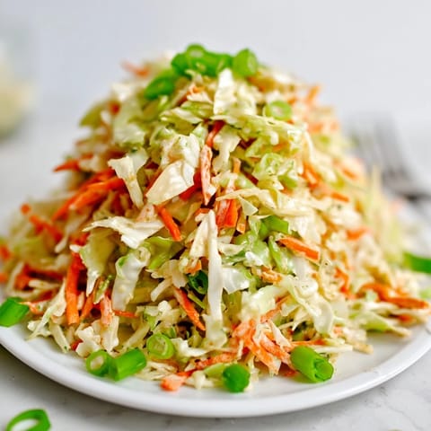 A vibrant bowl of Best Cabbage Coleslaw features a colorful mix of shredded green and red cabbage, carrots, and green onions tossed in creamy dressing.