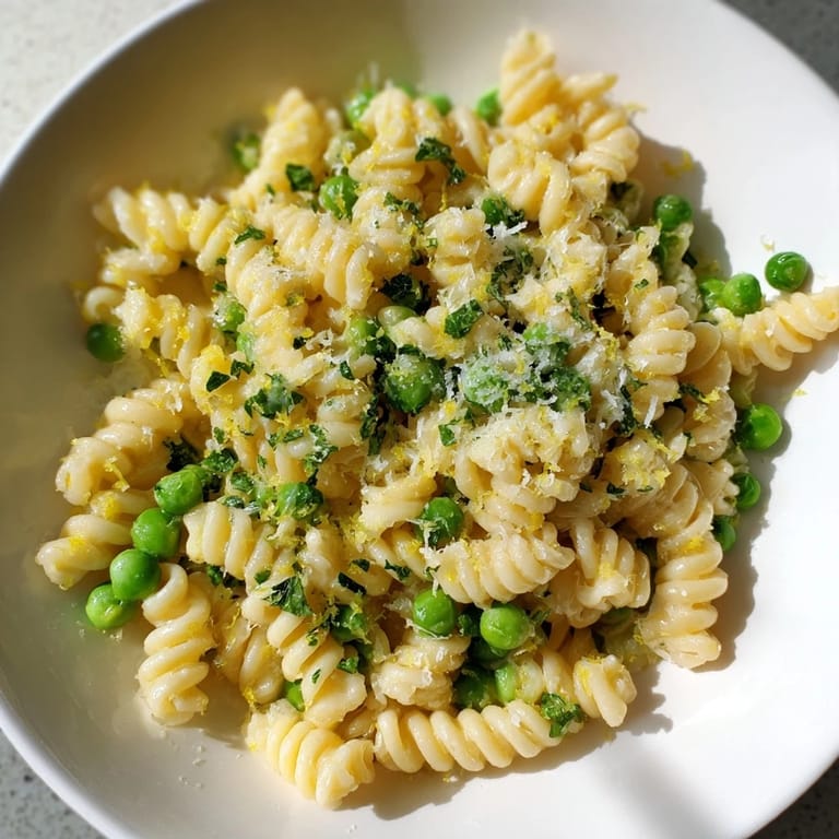 Tender ditalini pasta coated in garlic butter sauce with vibrant green peas in a close up photo.