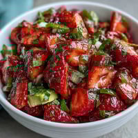 Fresh strawberry salsa with lime and jalapeño served in a white bowl, bursting with vibrant red berries, green herbs, and spicy peppers.